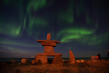 northern lights in churchill manitoba with an iconic inukshuk in the foreground