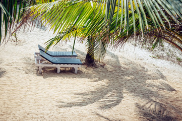 Sunbed under a palm tree on a hot sunny day. Shadow of palm leaves on the sand and empty sunbed. Waiting for tourists.