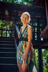 Portrait of young woman on blurry background on sunny summer day. Pretty blonde in a dress smiles at camera. Recreation, travel, vacation in tropical country.