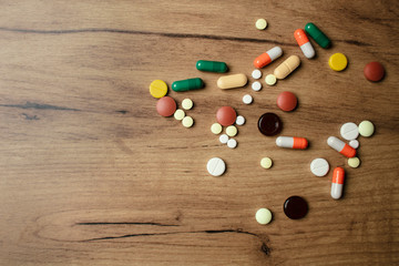 A handful of different pills on a wooden table. A lot of colorful different pills including anti-viral drugs. Medications against COVID-19 and other diseases.