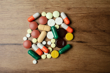 A handful of different pills on a wooden table. A lot of colorful different pills including anti-viral drugs. Medications against COVID-19 and other diseases.