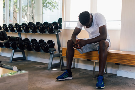 Desperate African American Male Athlete Sitting On Bench During Break In Fitness Training In Modern Gym