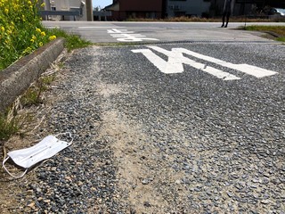 Discarded protective face mask beside the road in countryside Japan. The Japanese text on the road translates to 'stop'