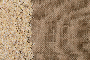 Oat flakes on a background of rough burlap. A diet rich in vitamins and nutrients.