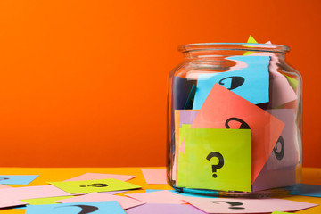 Colorful cards with question marks in glass jar on orange background. Space for text