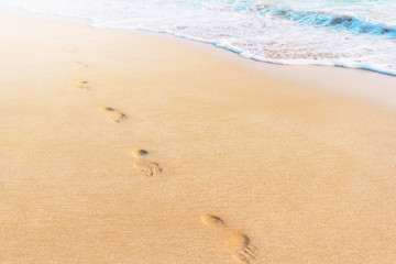 Fototapeta na wymiar Footprint in the sand in soft warm sunset light. Blue ocean wave and tropical beach. Concept photo.