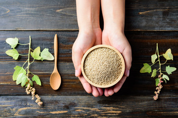 Organic raw brown quinoa seed in a bowl holding by hand on wooden background, healthy food