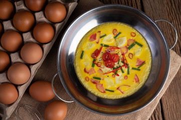 Steamed eggs with chili, spring onion and tomato in a pot and eggs in a panel on a wooden floor