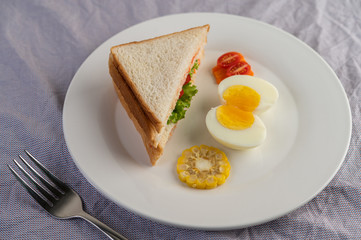 American breakfast on a white background with boiled eggs, corn, tomato and sandwich on a white plate.