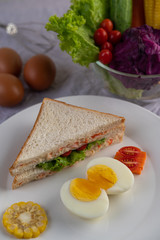 American breakfast on a white background with boiled eggs, corn, tomato and sandwich on a white plate.