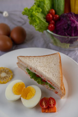 Fototapeta na wymiar American breakfast on a white background with boiled eggs, corn, tomato and sandwich on a white plate.