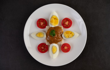 Bread topped with chili paste with boiled eggs and tomatoes on a white plate.