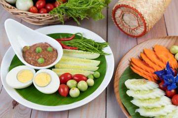 Chili paste paste in a bowl with eggplant, carrots, chili, cucumbers in a basket on wood table