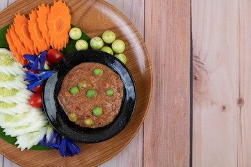 Chili paste paste in a bowl with eggplant, carrots, chili, cucumbers in a basket on wood table