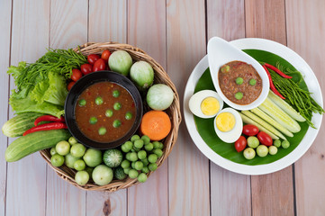 Chili paste paste in a bowl with eggplant, carrots, chili, cucumbers in a basket on wood table