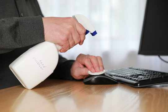 Unrecognizable man sanitizing workplace surfaces before using computer