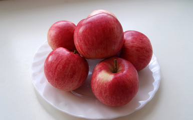 There are red apples on a white plate.