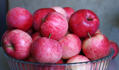 Fresh apples lie in a glass plate on a gray blurred background