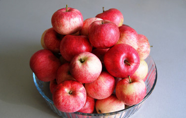Fresh apples lie in a glass plate on a gray blurred background