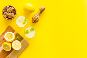 Homemade lemonade in glasses near juicer and cut lemons on yellow background top-down copy space