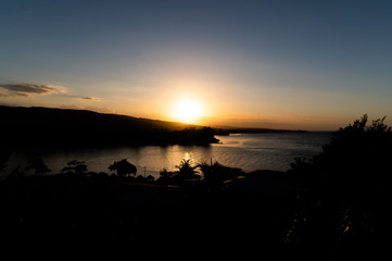 the orange sun cuts through the blue sky and embracing the mountains and kissing the ocean during a warm sunset by the beach