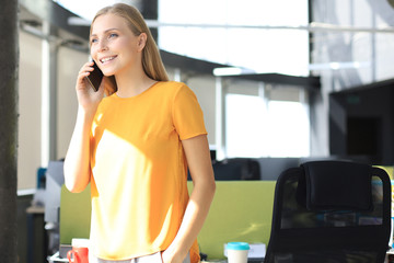 Attractive business woman talking with collegues on the mobile phone while sitting on the office desk