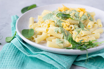 Penne pasta with green cream sauce, cheese and micro greens on a ceramic plate, light grey stone background. Italian food. Close up.