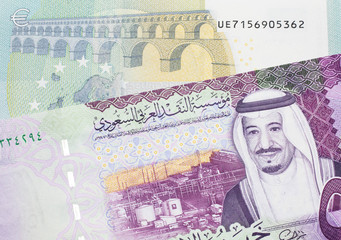 A green and yellow five Euro bank note from the EU with a colorful five riyal bank note from Saudi...