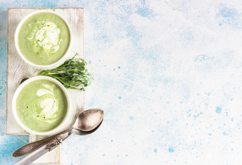 Detox cream soup of green vegetables (broccoli, green peas, spinach) served with cream, lemon zest and micro greens on grey concrete background. Clean eating, healthy food concept. Top view. 