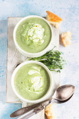 Detox cream soup of green vegetables (broccoli, green peas, spinach) served with cream, lemon zest and micro greens on grey concrete background. Clean eating, healthy food concept. Top view. 
