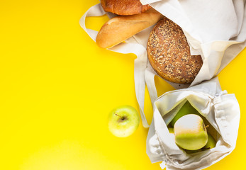 Reusable zero waste textile bag with bread and green apples in handmade reusable canvas bag on a yellow paper background. Top view with copy space.