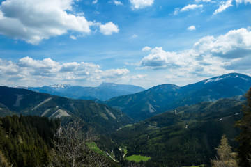 A vast view on Alpine valley from the upper parts of Himmeleck in Austria. The valley is lush green. There are many mountain ranges in the back. Spring coming to the Alps. Dense forest