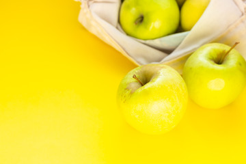 Reusable cotton textile bag with green apples on a yellow paper background. The concept of zero waste, ecology shopping. 