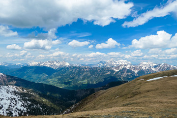 A vast view on Alpine valley from the upper parts of Himmeleck in Austria. The valley is lush green. There are many mountain ranges in the back, covered with snow. Spring coming to the Alps.