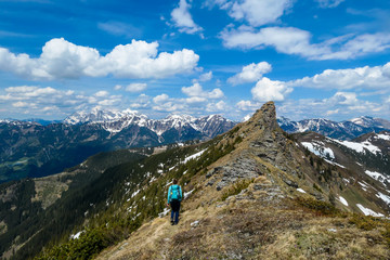 Fototapeta premium A woman with big hiking backpack hiking to Himmeleck peak, Austrian Alps. There is a massive mountain range in the back, partially covered with snow. Early spring vibes. Freedom and adventure.