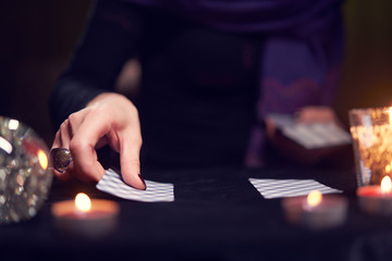 Close-up of fortuneteller's hands with fortune-telling cards at table with candles