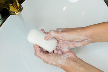 Man or woman washing hands, rubbing with soap in sink under water. Hand disinfection. Close up...