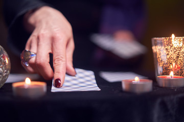 Close-up of fortuneteller's hand with fortune-telling cards at table with candles in dark room