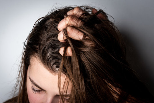 Young woman with dirty greasy hair on gray background. 