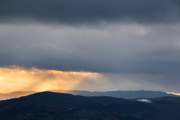 Sunrays coming over mountains beneath moody clouds