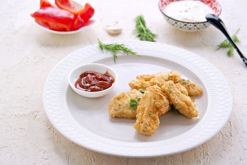 Chicken nuggets on a white plate on a light concrete background. Served with ketchup and mayonnaise, yogurt and grainy mustard sauce. Food for parties. American cuisine. Copyspace