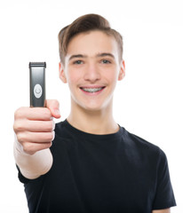 Smiling Teenage boy holds an electric razor in his hands, looking at camera - isolated on a white background