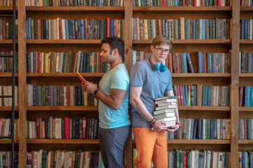 Two young men standing in the library back to back