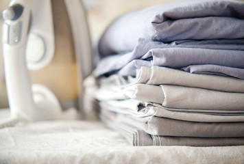 pile of bed clotheth or bed linen and iron. home work concept. monochrome gradient white gray blue bed linen textiles clothing.