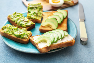Plate with tasty avocado sandwiches on color background