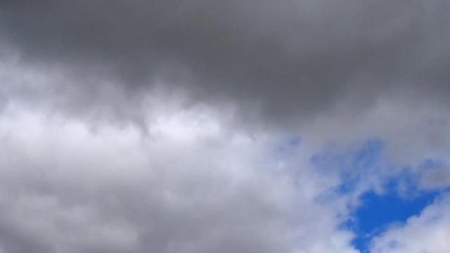 Time lapse of gray and white dark rain clouds moving through the sky with a patch of blue
