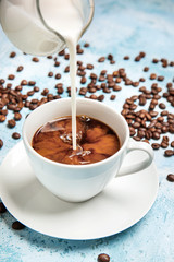 Pouring of milk in cup of hot coffee on table