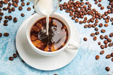 Pouring of milk in cup of hot coffee on table