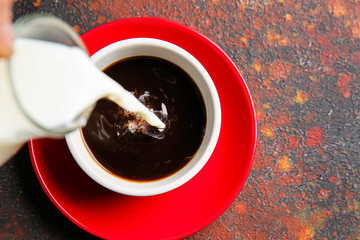 Pouring of milk in cup of hot coffee on table