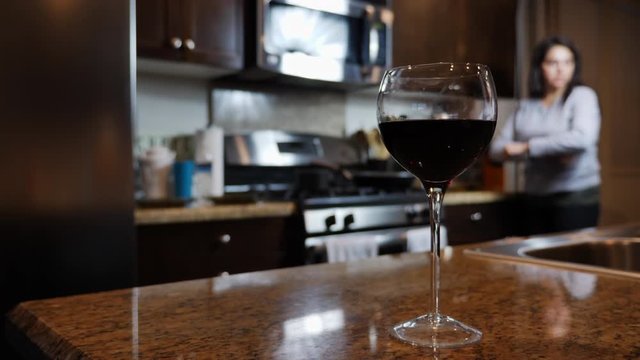 Woman standing in kitchen alone in self-isolation with red wine glass in focus